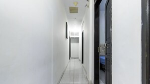 A narrow, well-lit hallway with white walls and a tiled floor, leading to a room with a dark door and a visible window. - Reddoorz near Gajah Mada Plaza 2 (Jakarta)