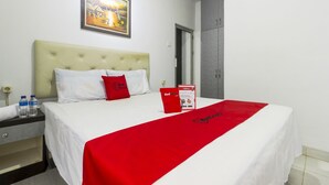 A hotel room with a bed, a nightstand, a water bottle, a red pillow, a framed picture on the wall, and a wardrobe. - Reddoorz near Gajah Mada Plaza 2 (Jakarta)