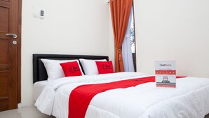 A neatly made bed with white and red bedding, a wooden door, and a RedDoorz sign on the bed. - RedDoorz @ Pasir Luyu Buahbatu (Bandung)