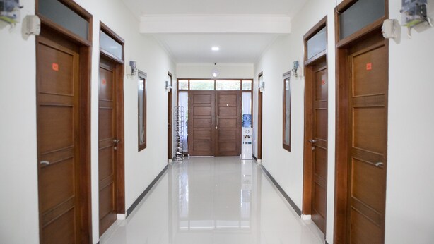 A hallway with wooden doors, a water dispenser, and a ceiling light. - RedDoorz @ Pasir Luyu Buahbatu (Bandung)