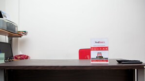 A wooden desk with a RedDoorz sign, a remote control, and a tissue box. - RedDoorz @ Pasir Luyu Buahbatu (Bandung)