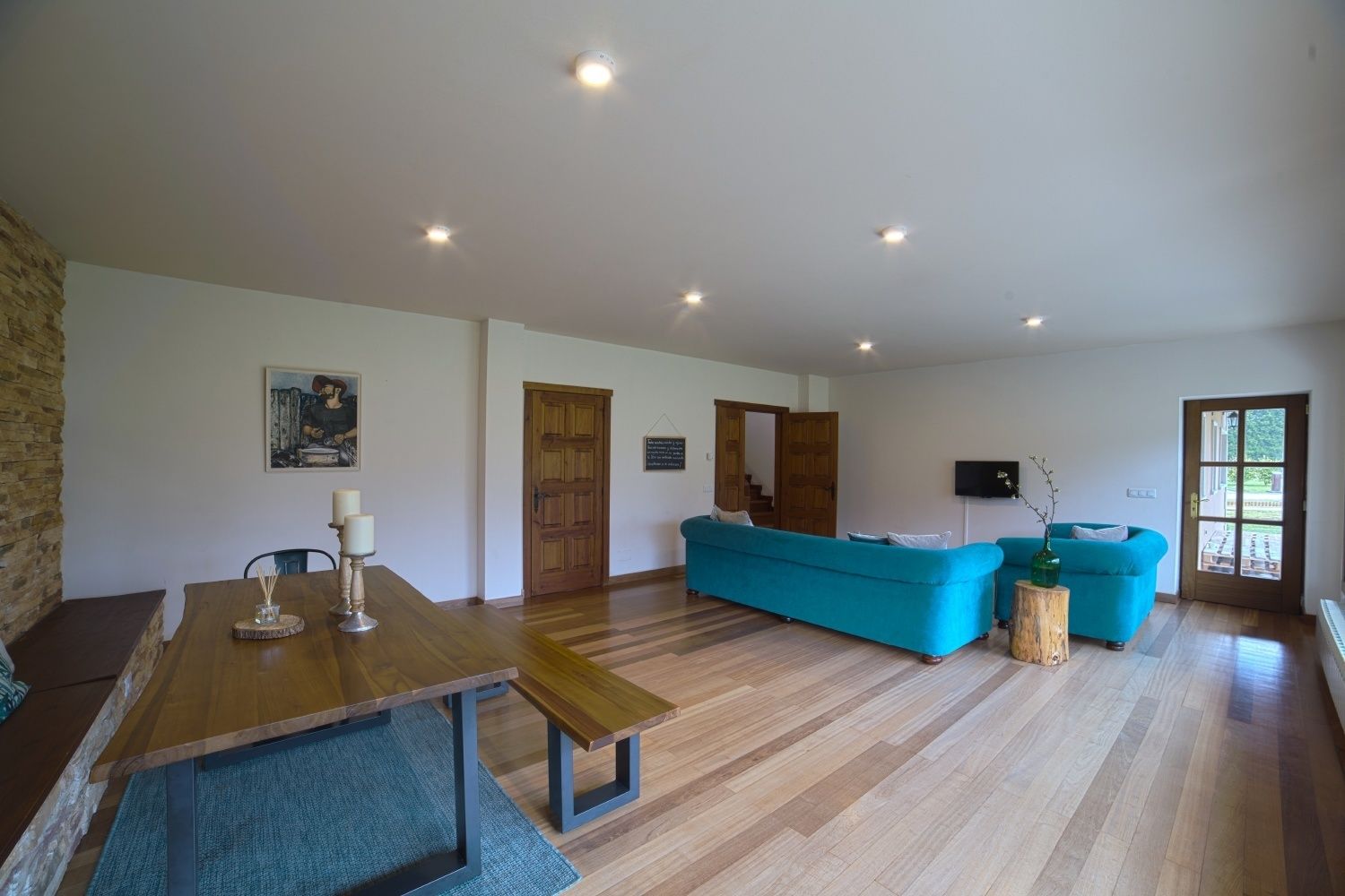 A spacious living area with a wooden dining table, a blue sofa, and a wooden bench.