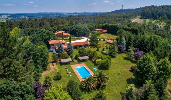 An aerial view of a residential area with multiple houses, a swimming pool, and surrounding greenery.