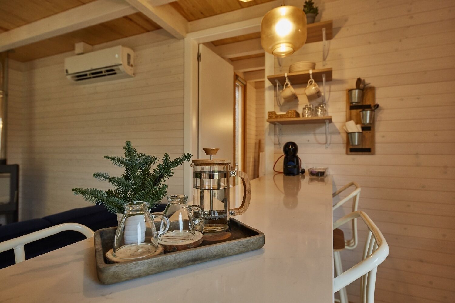 A wooden interior with a kitchen area, a dining table with a tray of items, and a hanging light fixture.