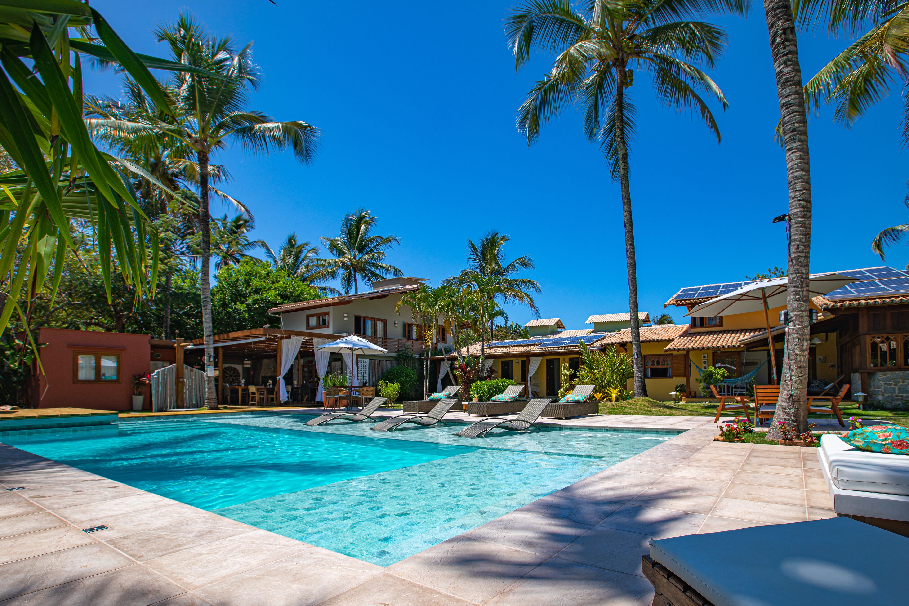 A swimming pool with lounge chairs, palm trees, and a building with a tiled roof.