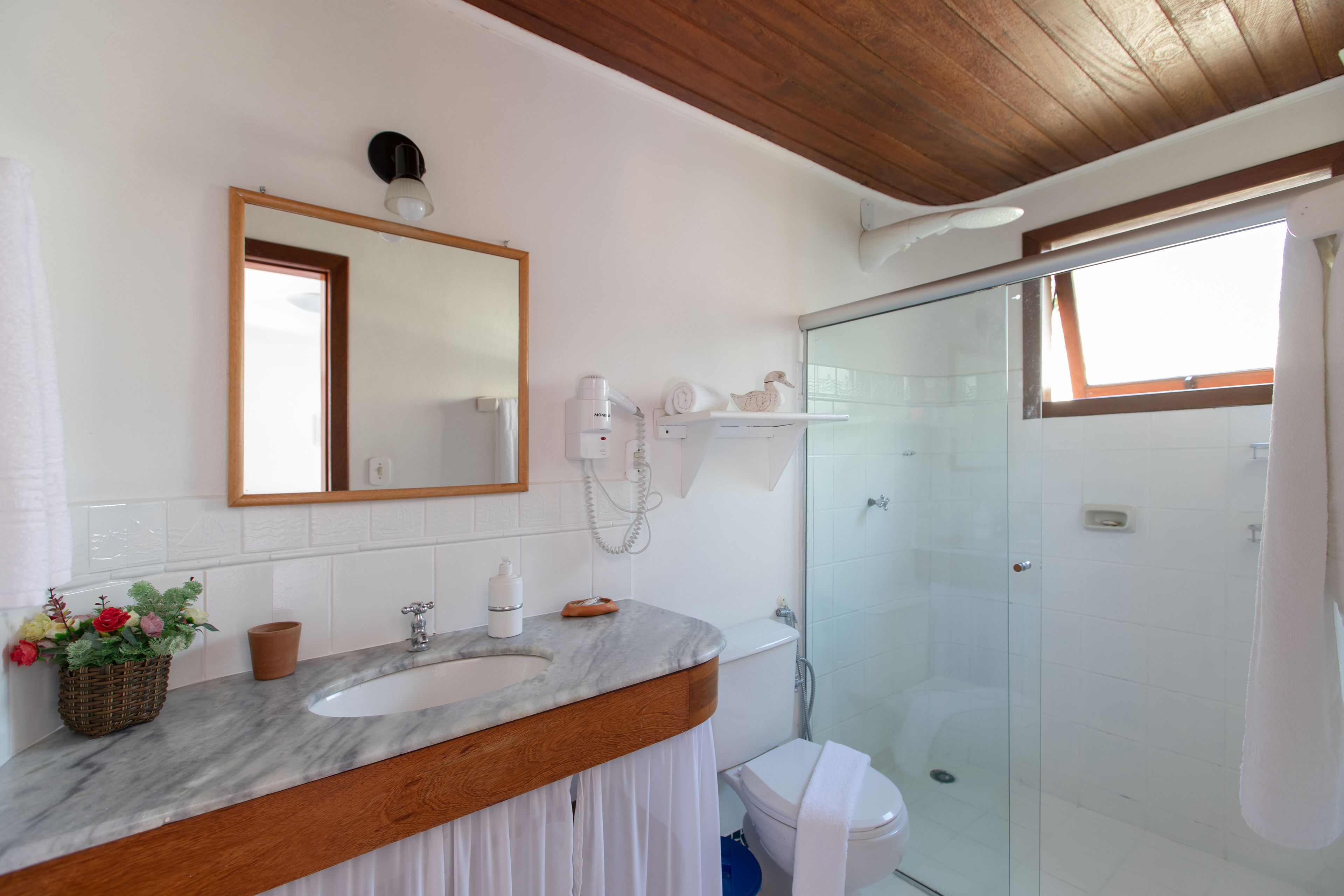 Une salle de bain avec un lavabo en marbre, un meuble-lavabo en bois, une cabine de douche en verre et un grand miroir.