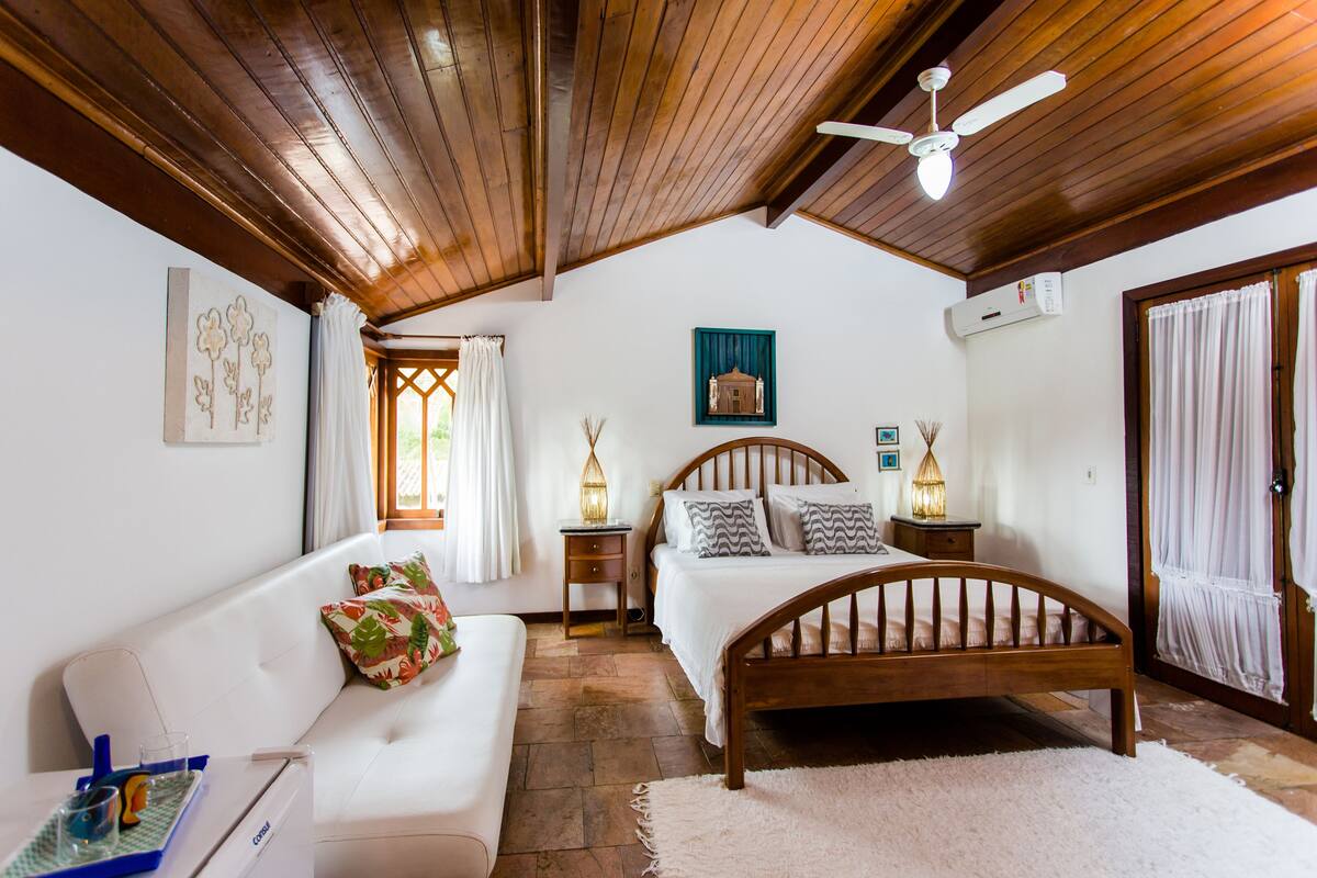 A bedroom with a wooden ceiling, a bed with a wooden headboard, a white sofa, and a small table with a tray.