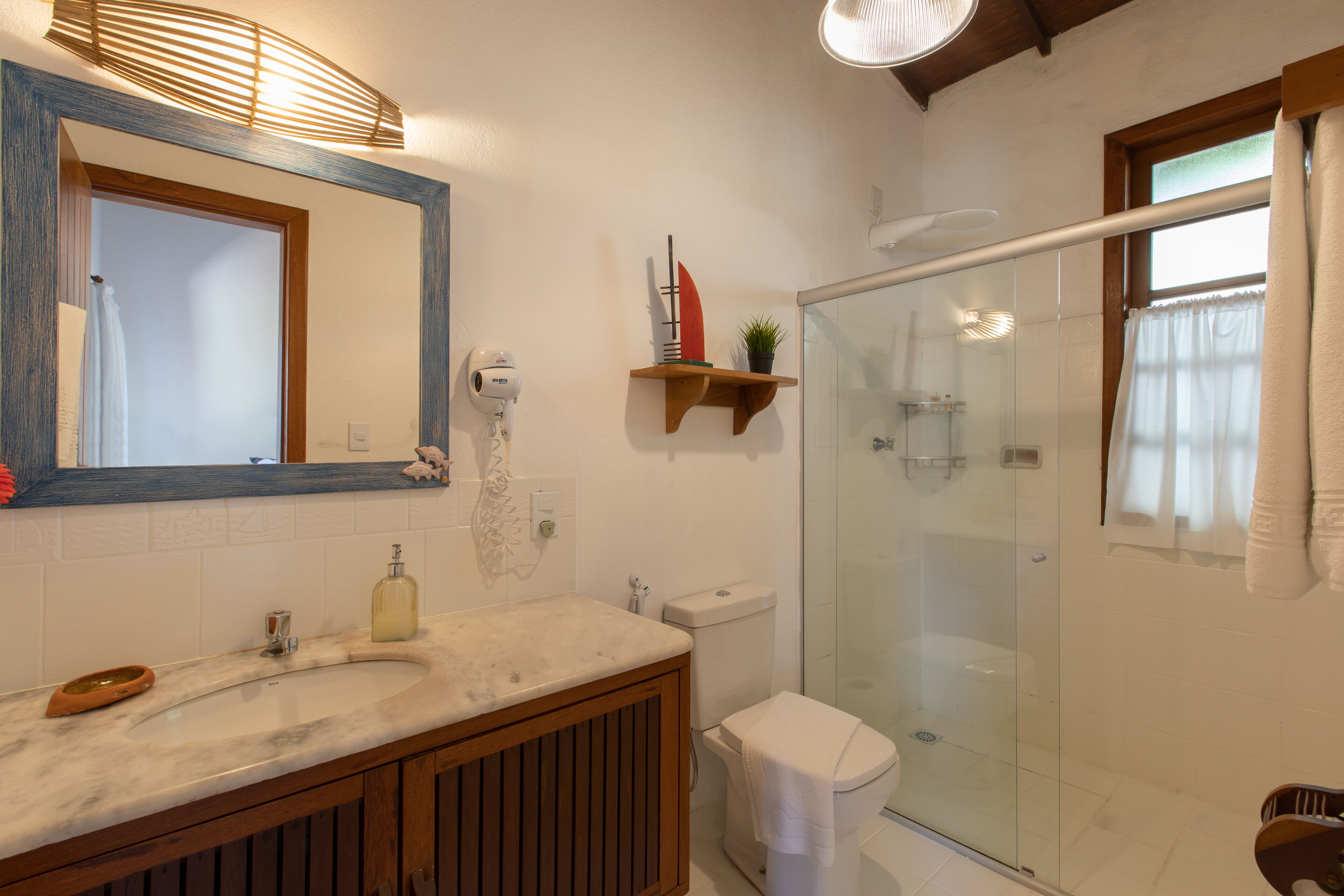A bathroom with a marble sink, wooden vanity, a glass shower enclosure, and a mirror with a wooden frame.
