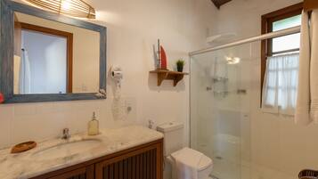 A bathroom with a marble sink, wooden vanity, a glass shower enclosure, and a mirror with a wooden frame.
