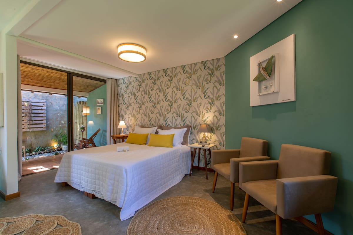 A bedroom with a bed, two chairs, a bedside table with a lamp, and a wall-mounted picture.