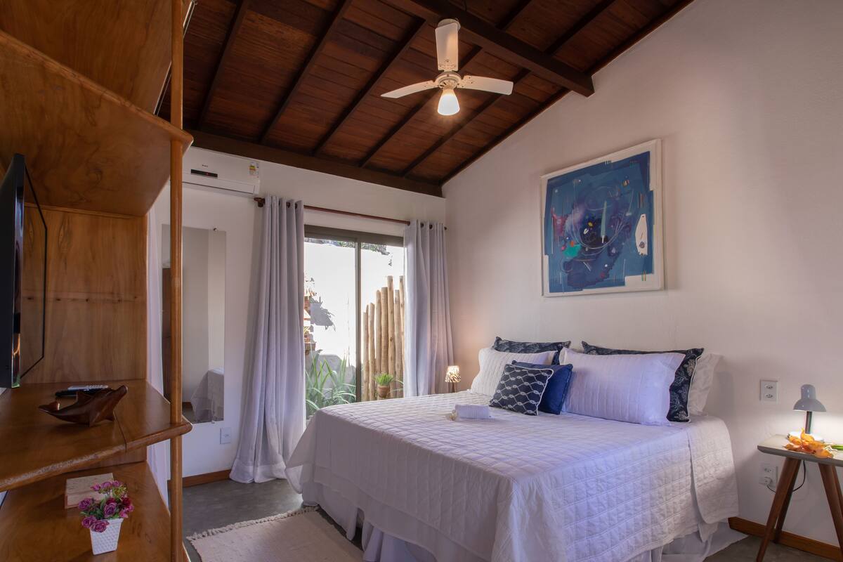 A bedroom with a bed, a ceiling fan, a painting, and a window with curtains.