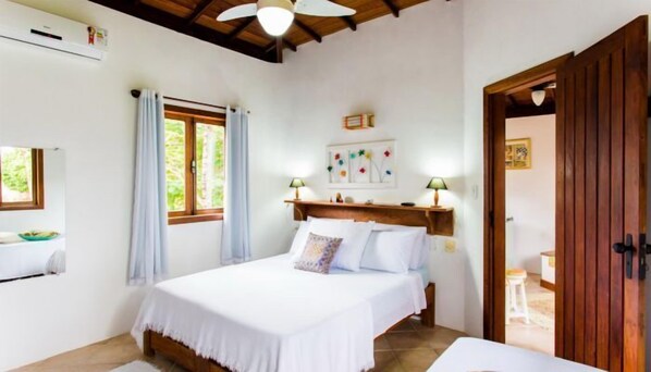 A bedroom with a bed, a nightstand, a window with curtains, a ceiling fan, and a wooden door.