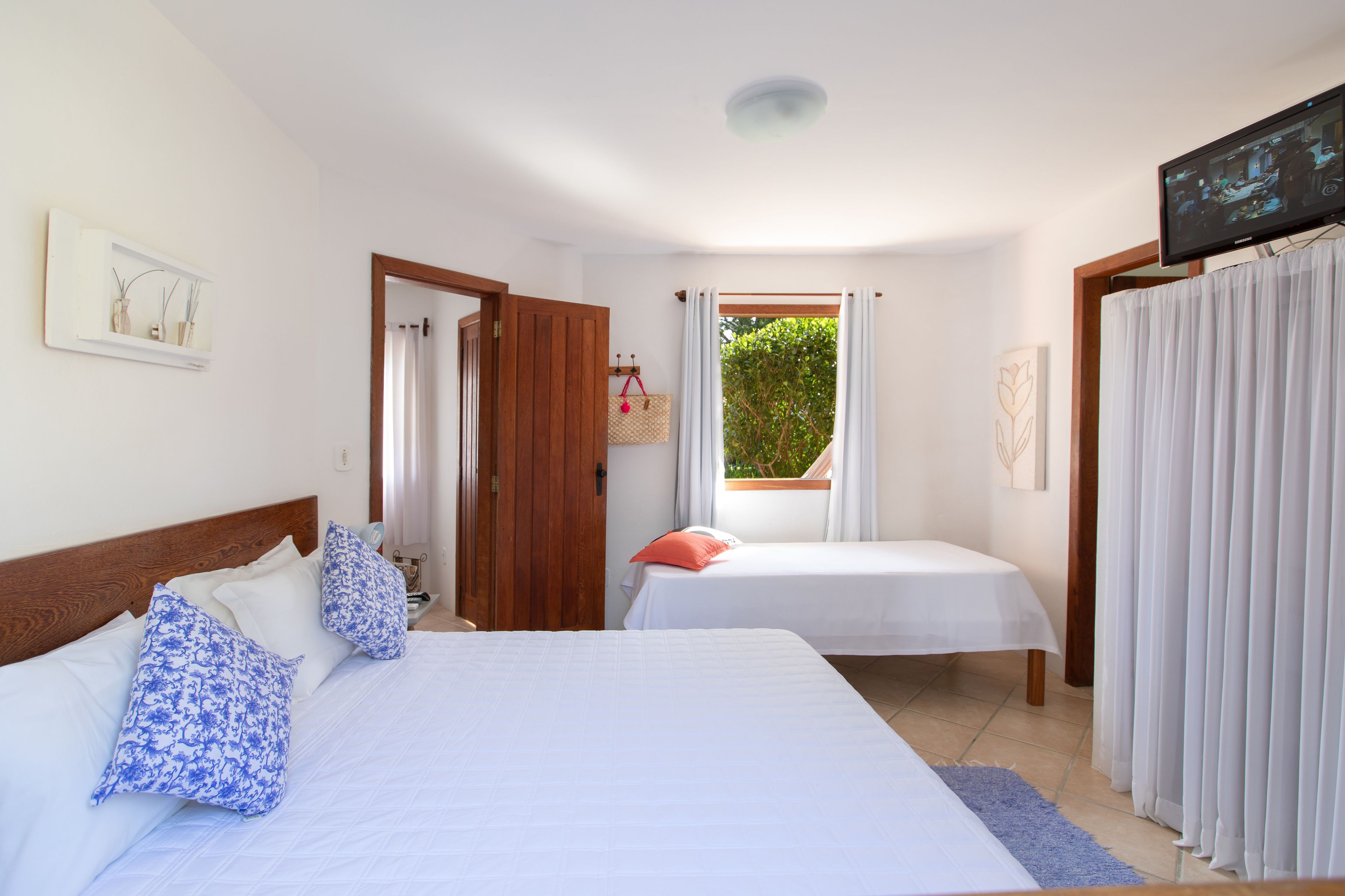 A hotel room with two beds, a television, a window with curtains, and a door leading to another room.