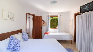 A hotel room with two beds, a television, a window with curtains, and a door leading to another room.