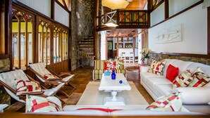 A spacious room with a white sofa, lounge chairs, a dining table, and a staircase leading to an upper level. - Recanto do Arraial - Pousada (Porto Seguro)