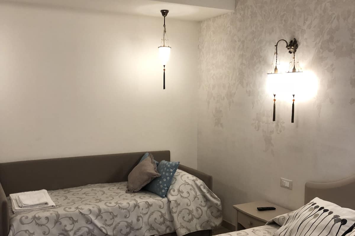A hotel room with two beds, a nightstand, and wall-mounted lighting.