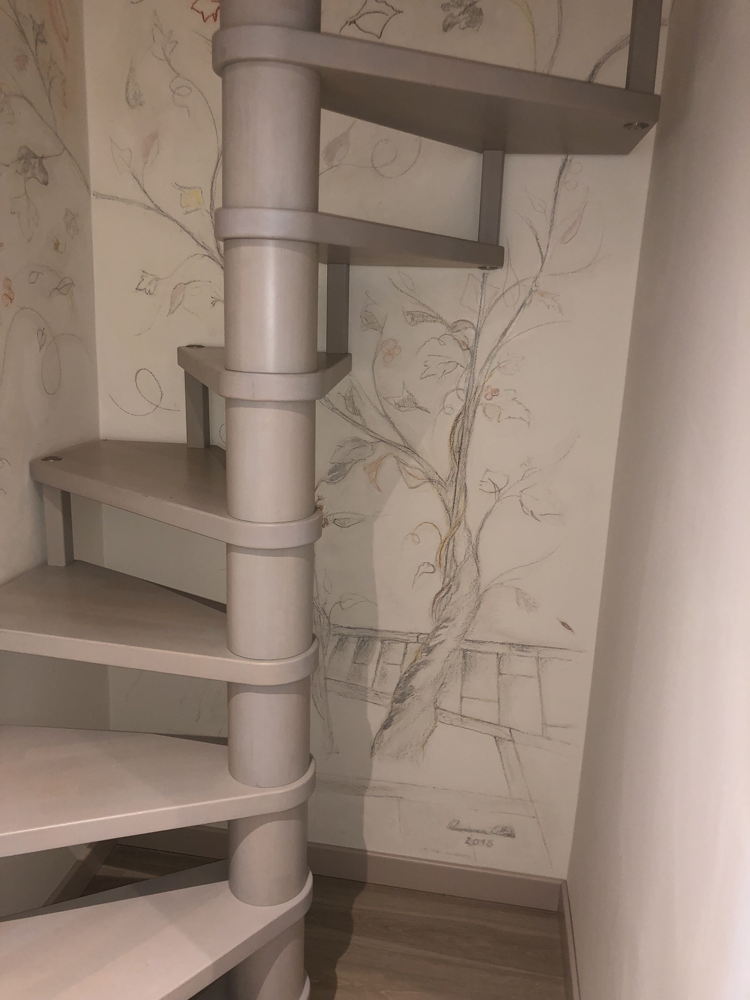 A corner of a room with a grey, spiral staircase leading to a higher floor.