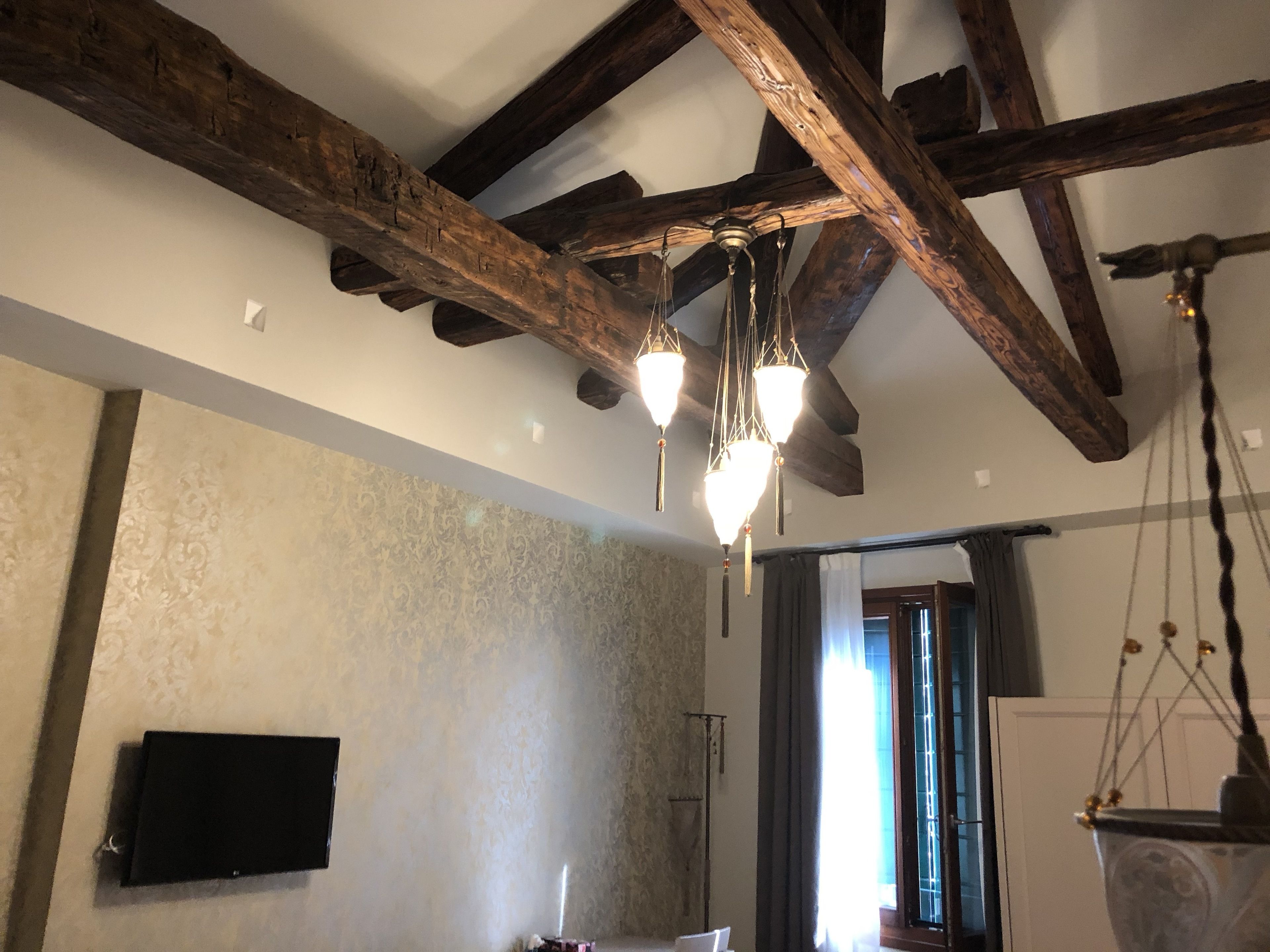 Een kamer met zichtbare houten balken, een patroonmuur, een flatscreen televisie en een hanglamp.