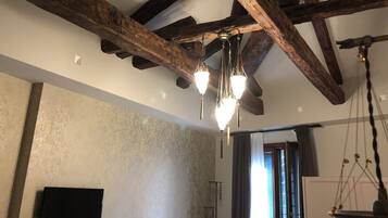 Een kamer met zichtbare houten balken, een patroonmuur, een flatscreen televisie en een hanglamp.
