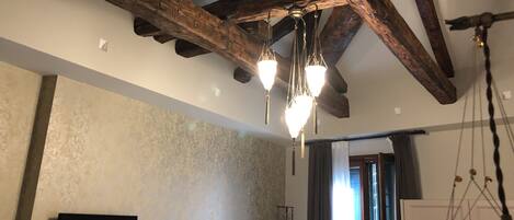 A room with exposed wooden beams, a patterned wall, a flat-screen TV, and a hanging light fixture.