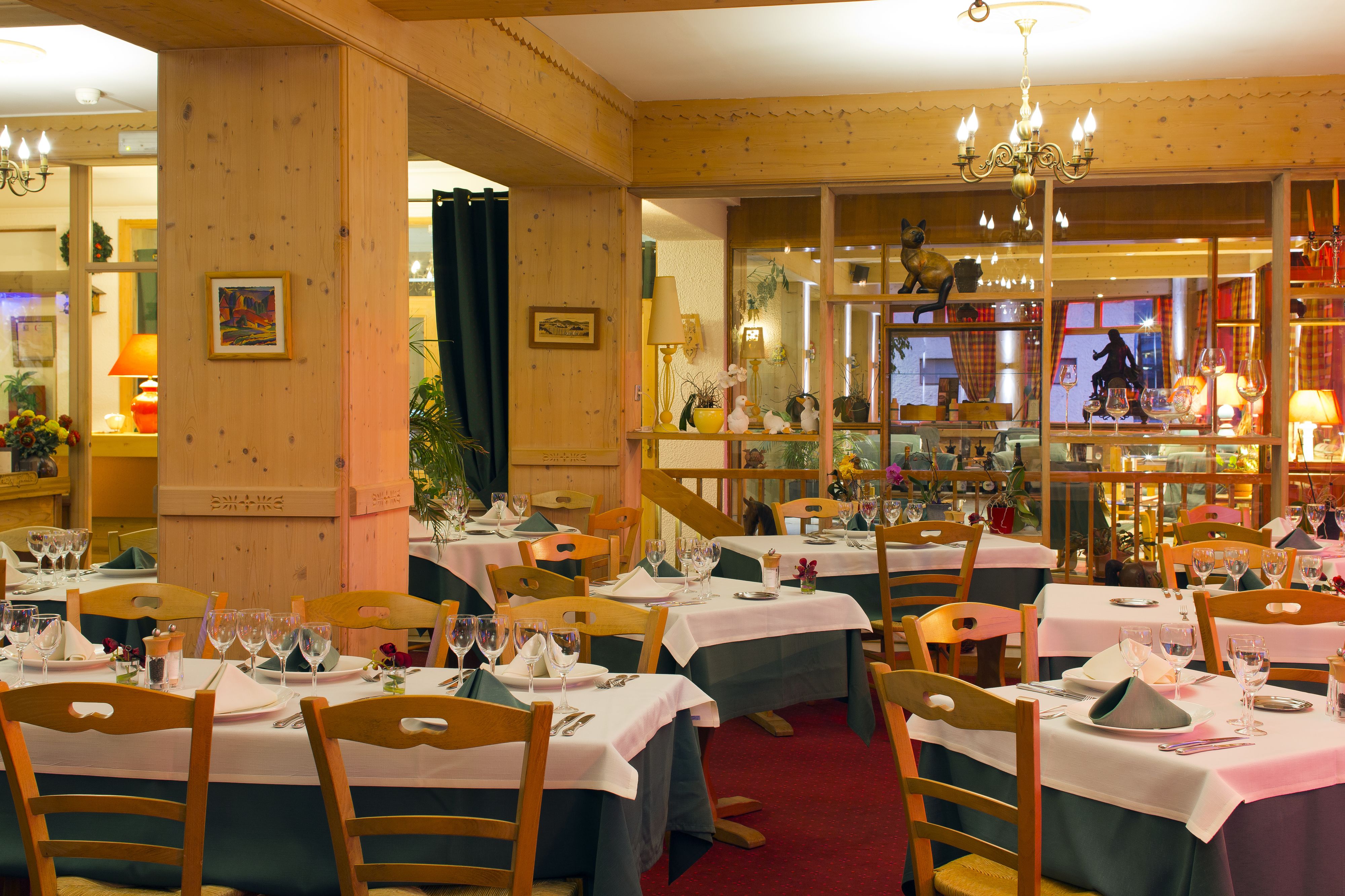 A restaurant with multiple tables set for dining, wooden chairs, and a chandelier.