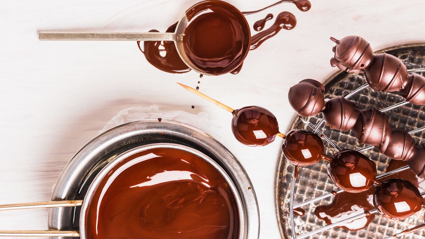A metal container with a liquid, a ladle, and chocolate-covered items on a rack.