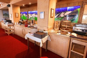 A buffet setup with a variety of food items and drinks, wooden paneling, and artwork on the walls. - Hôtel Le Castillan (Huez)