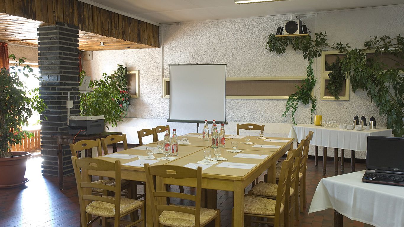 Un salón de conferencias con una pizarra, mesas de madera, sillas y plantas en macetas.