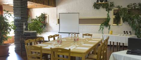 Un salón de conferencias con una pizarra, mesas de madera, sillas y plantas en macetas.