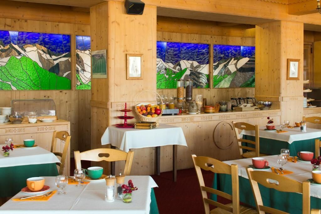 A restaurant with wooden walls and green tablecloths. There are wooden chairs and tables set up for dining.