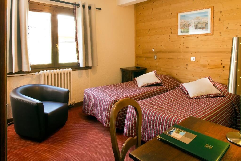 Habitación con dos camas, una silla, una mesa, un radiador y una ventana con cortinas.