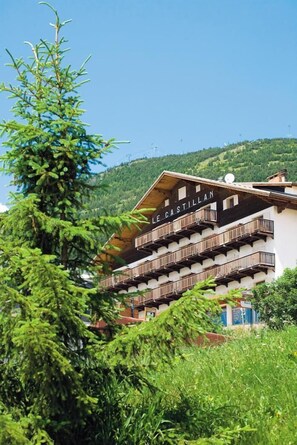 A multi-story building with balconies, labeled "LE CASTILLAN," surrounded by greenery and a mountainous backdrop. - Hôtel Le Castillan (Huez)
