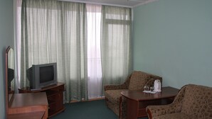 A room with a television on a wooden stand, a sofa, a small table with a kettle, and a window with sheer curtains. - Tourist Hotel (Lviv)