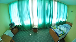 A room with a bed, a small table, a TV, and curtains. - Tourist Hotel (Lviv)