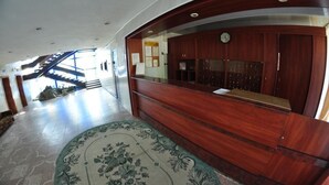 A reception area with a wooden reception desk, a clock, and a staircase leading to an upper floor. - Tourist Hotel (Lviv)