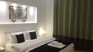A neatly made bed with white linens and a black throw, a bedside lamp, and a wall-mounted artwork above the bed.
