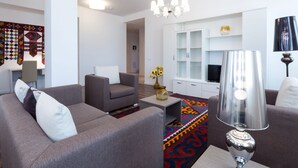 A modern living room with grey sofas, a coffee table, a chandelier, and a TV.
