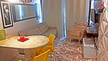 A compact living space with a sofa, a dining table with chairs, a television, and a small cabinet.