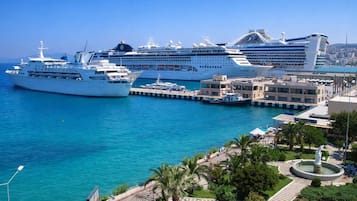 Eine Marina mit mehreren vor Anker liegenden Kreuzfahrtschiffen, einer Promenade mit Palmen und einem klaren, blauen Meer.