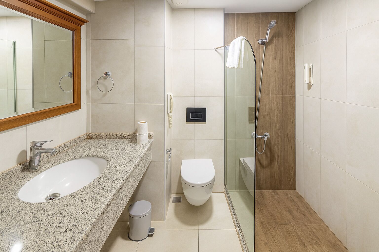 A bathroom with a granite countertop sink, a toilet, and a glass-enclosed shower.