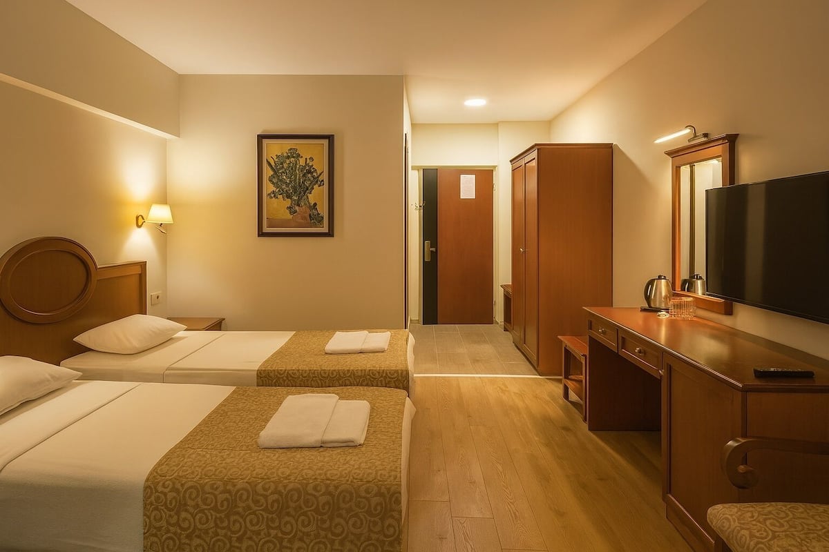 Ein Hotelzimmer mit zwei Betten, einem Schreibtisch mit Fernseher, einem Spiegel und einem Bild an der Wand.