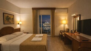 A hotel room with a bed, a desk, a chair, a TV, and a view of a cruise ship. - Kayhanbey Otel (Kuşadası)