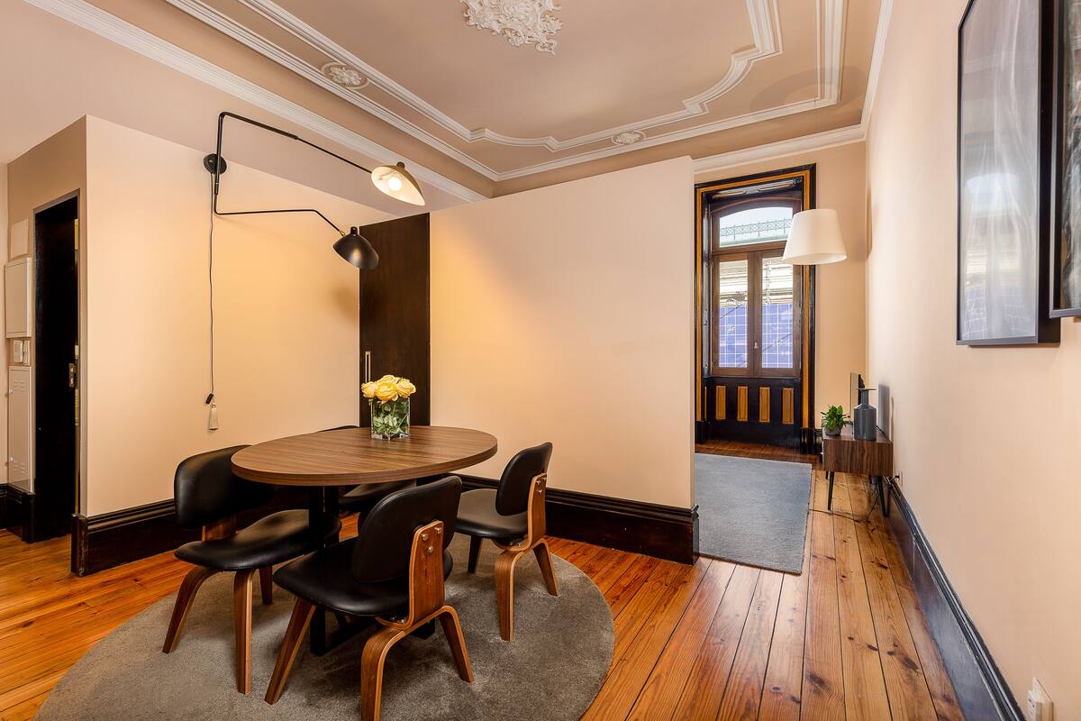 A dining area with a round table, four chairs, a vase with flowers, and a lamp.