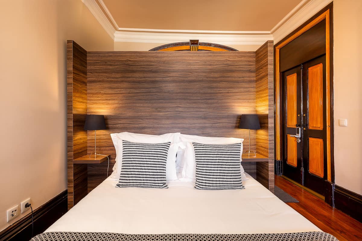 A hotel room with a large bed, two bedside lamps, a wooden headboard, and a door with a wooden panel.