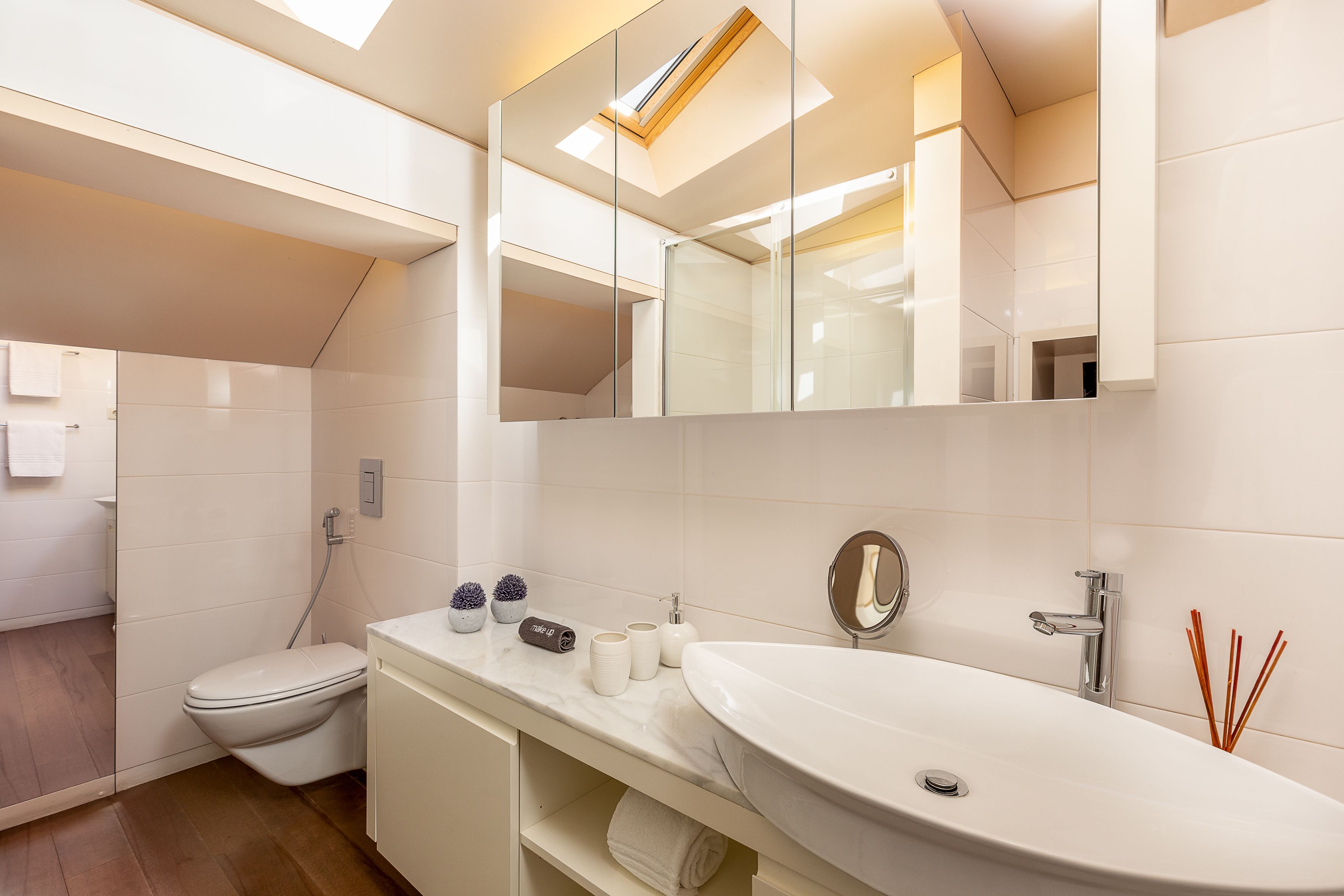 A modern bathroom with a white sink, mirror, and toilet.