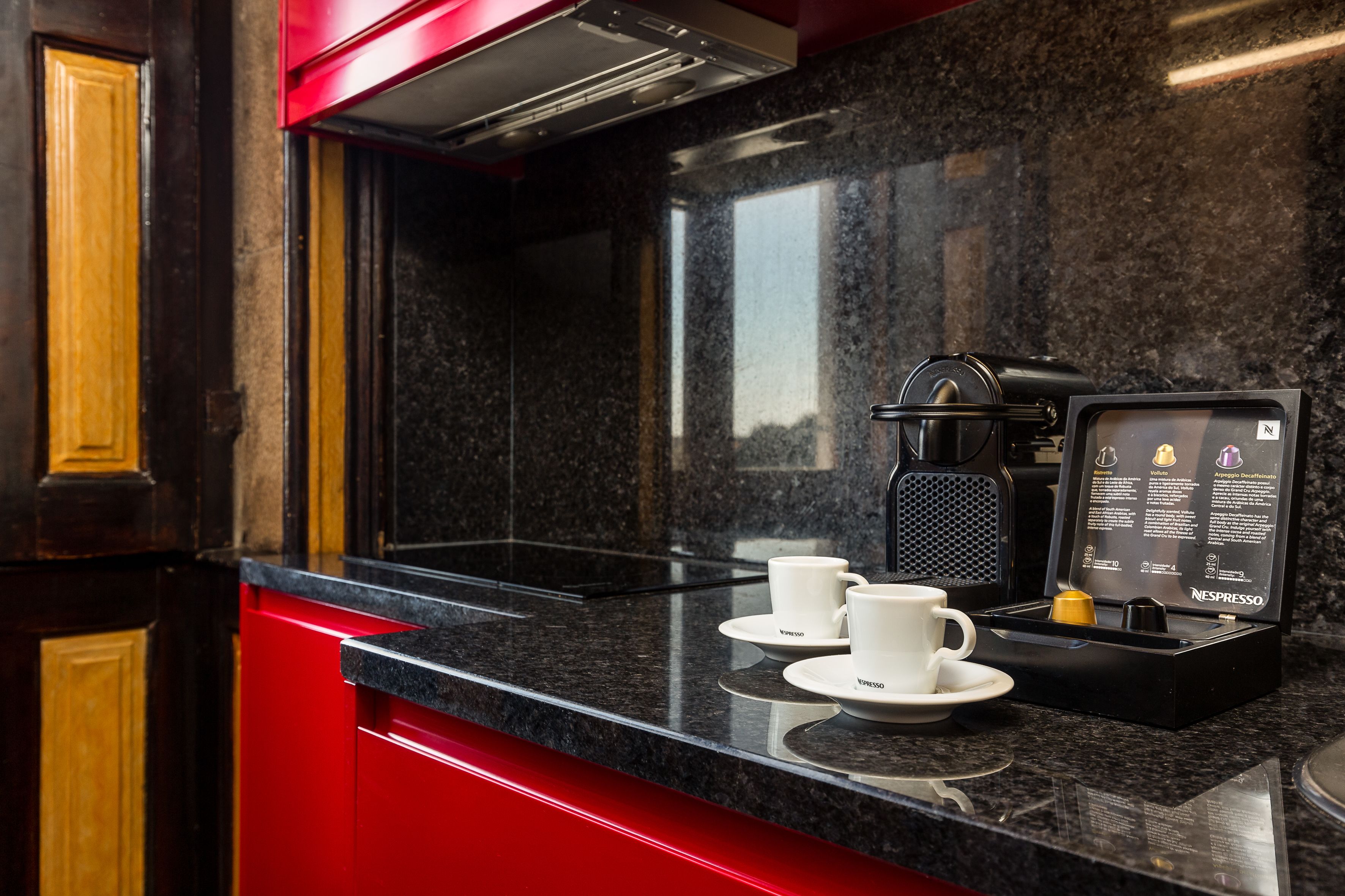 Una cocina moderna con encimera negra, dos tazas blancas, una máquina Nespresso y un expositor de menú.