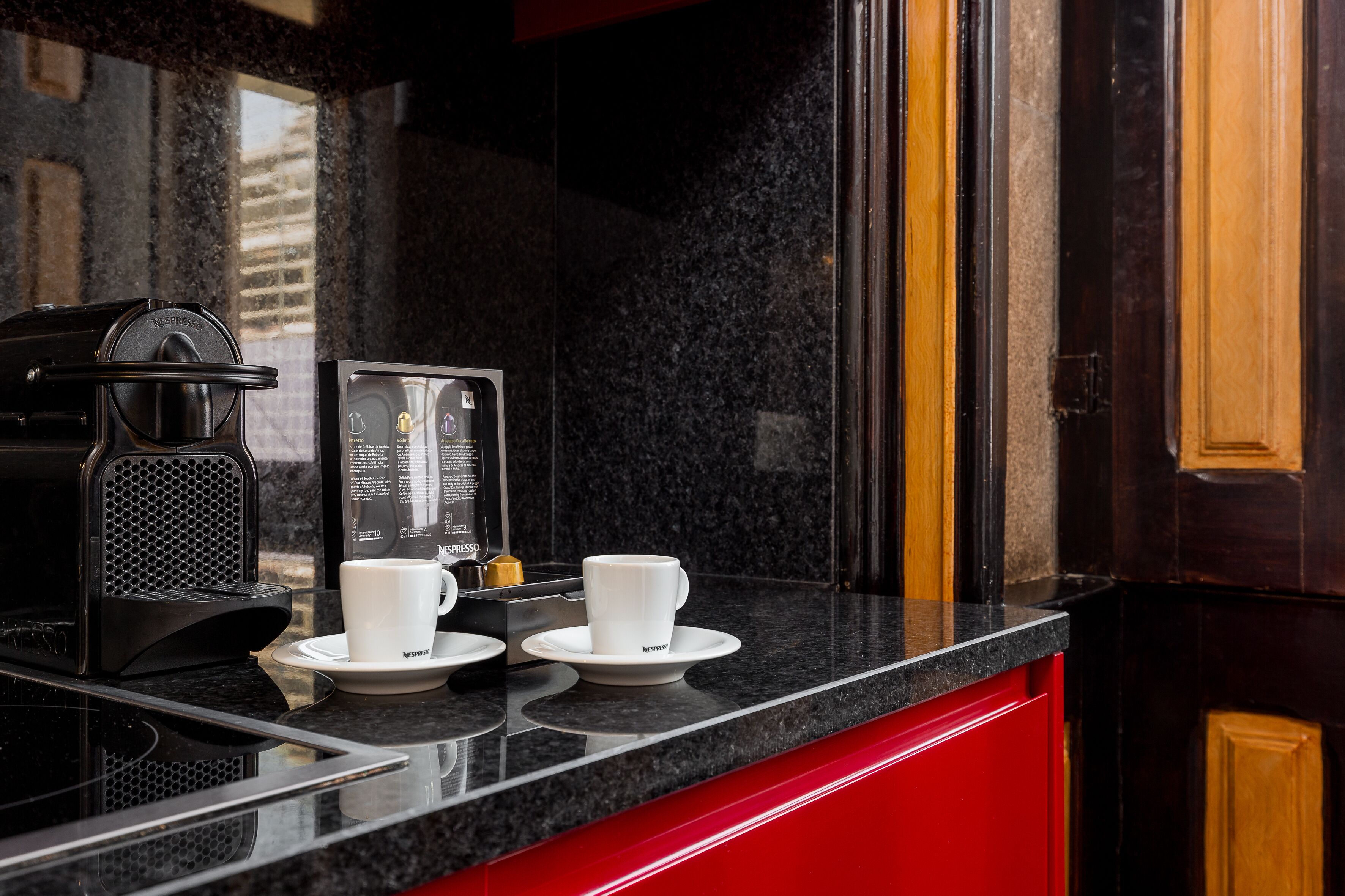 A modern kitchen with a black countertop, a coffee machine, and two white cups on a matching saucer.
