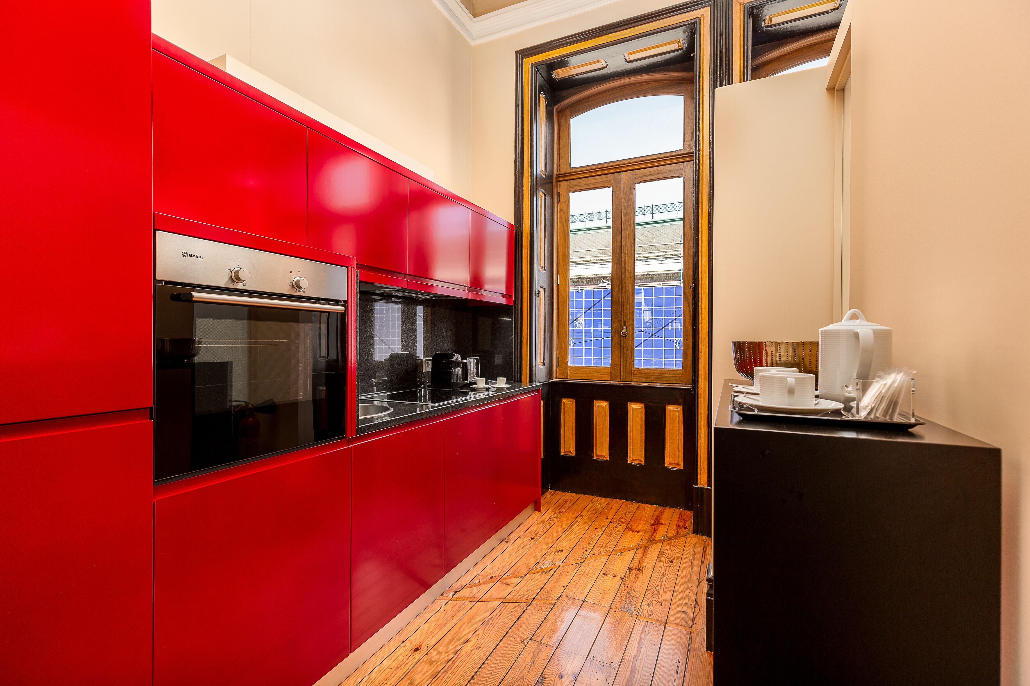 A modern kitchen with red cabinets, a built-in oven, and a wooden floor.