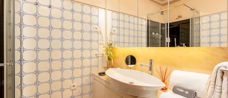 A modern bathroom with a large mirror, a white sink, and a tiled wall with a geometric pattern.