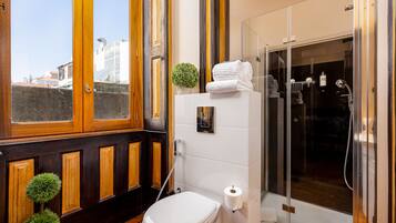 Un bagno moderno con un mobile bagno in legno, un water, un box doccia in vetro e vista sulla città da una grande finestra.